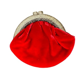 Puede incluir: Un monedero de terciopelo rojo con un cierre de purpurina dorada. El monedero tiene forma redondeada y cierre de beso. El interior del monedero no es visible.