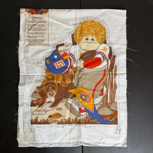 May include: A vintage fabric panel featuring a cartoon illustration of a child in a football uniform holding a football and a helmet. A dog is on a leash. The panel includes instructions and the text "LEAVE OPEN FOR STUFFING".