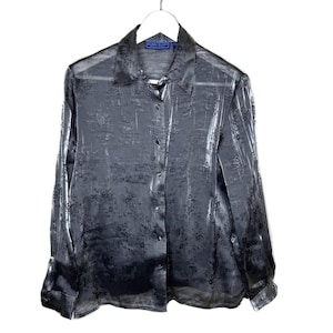 May include: A sheer, long-sleeved button-down shirt in a dark gray color, hanging on a white hanger. The shirt has a subtle floral pattern and a collared neckline. The label reads "Karen Scott".