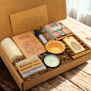 May include: A gift box filled with self-care items. Includes a handmade soap, facial mask, essential oil, candle, lip balm, wooden bowl, and a decorative wooden tag. The box also contains a handwritten card with a birthday message.