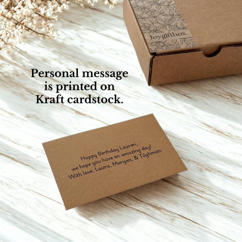 May include: A brown gift box with a floral design on the lid and the text "joygiftbox". A Kraft cardstock card with a personalized message is visible. The text on the card reads "Happy Birthday Lauren, we hope you have an amazing day! With love; Laura, Morgan, & Tilghman."