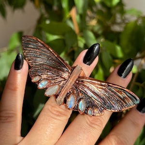 May include: A copper butterfly ring with iridescent moonstone accents and a clear quartz crystal in the center.