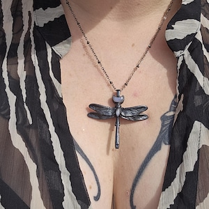 May include: A silver chain necklace with a dragonfly pendant. The dragonfly is made of metal and has a light blue gemstone in its body.