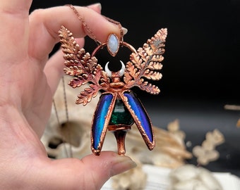 May include: Copper pendant necklace featuring a green and blue beetle with fern wings and a moonstone accent.