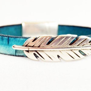 May include: A turquoise leather bracelet with a silver feather charm. The bracelet is made of genuine leather and has a magnetic clasp.
