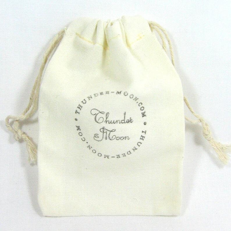May include: A white cotton drawstring bag with a silver logo that reads "Thunder & Moon.com".