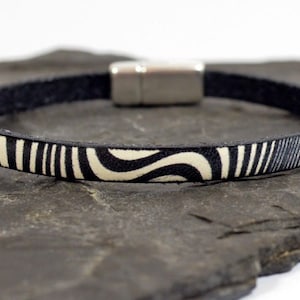 May include: A black leather bracelet with a white and black geometric pattern. The bracelet has a magnetic clasp.