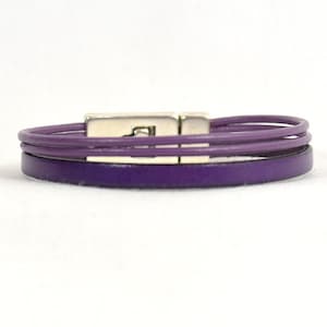 May include: A purple leather bracelet with a silver clasp. The bracelet is made of three strands of leather.