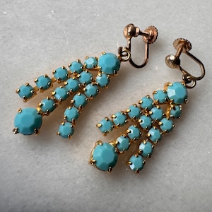 May include: A pair of gold tone clip-on earrings with turquoise blue glass stones. The earrings are in the shape of a teardrop with multiple rows of stones.