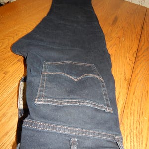 Pode incluir: Cal&ccedil;as de ganga azul escuro com um design cl&aacute;ssico de cinco bolsos. As cal&ccedil;as t&ecirc;m um corte de perna reto e est&atilde;o dobradas sobre uma superf&iacute;cie de madeira. O bolso traseiro tem um padr&atilde;o de costura distinto. A etiqueta da marca &eacute; vis&iacute;vel.