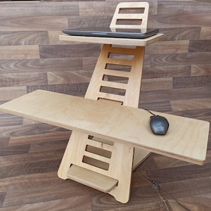 May include: A wooden standing desk with a laptop on the top shelf and a mouse on the lower shelf. The desk is made of light wood and has a simple design.