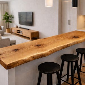 Può includere: Un piano bar in legno naturale con bordo a vivo, sostenuto da una base bianca. Tre sgabelli neri sono posizionati di fronte. Il bar si trova in un moderno spazio abitativo con divano, TV e palette di colori neutri.