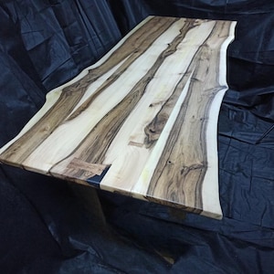 Könnte beinhalten: Handgefertigter Holztisch mit einer Baumkante. Die Tischplatte weist abwechselnd helle und dunkle Holzmaserungsmuster auf. Der Tisch wird von Holzbeinen getragen und ist etwa 180 cm lang und 80 cm breit.