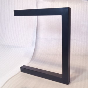 Könnte beinhalten: Schwarzes Metalltischbein mit quadratischer Form. Das Bein besteht aus dickem, robustem Metall und hat eine glatte, schwarze Oberfläche.