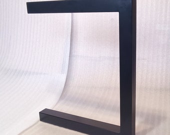 Könnte beinhalten: Schwarzes Metalltischbein mit quadratischer Form. Das Bein besteht aus dickem, robustem Metall und hat eine glatte, schwarze Oberfläche.