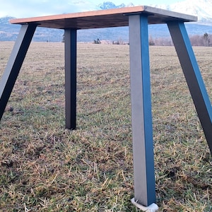 Könnte beinhalten: Ein Holztisch mit schwarzen Metallbeinen. Der Tisch steht auf einer grasbewachsenen Wiese.