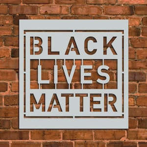 May include: A white stencil with the words "Black Lives Matter" in black lettering. The stencil is on a brick wall background.