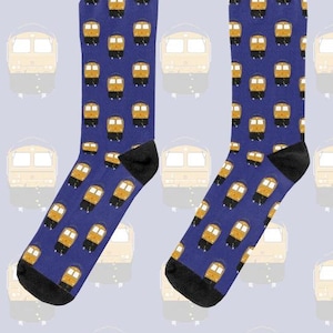 May include: A pair of blue socks with a repeating pattern of yellow and black train car illustrations. The socks have black heels and toes. The background features a faded train car design.