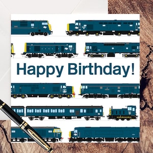 May include: A white envelope and a greeting card with a train theme. The card features multiple illustrations of blue trains with the text "Happy Birthday!" A black and gold pen rests on the wooden surface.