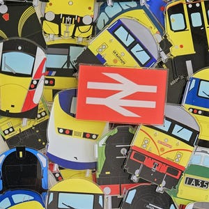 May include: A collection of colorful train-themed stickers featuring various train designs. The stickers include yellow, red, blue, and black trains, with a red and white British Rail logo in the center.