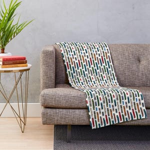 May include: A white throw blanket draped over a gray sofa, featuring a repeating pattern of colorful vertical rectangles in shades of red, green, blue, and brown. The blanket adds a decorative touch to the living room.