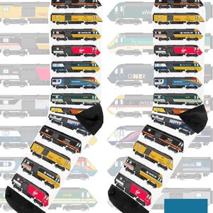 May include: A pair of white socks with black heels and toes, patterned with illustrations of various colorful trains. The trains are in different designs and colours. The text "On The Rails" is in a blue box.