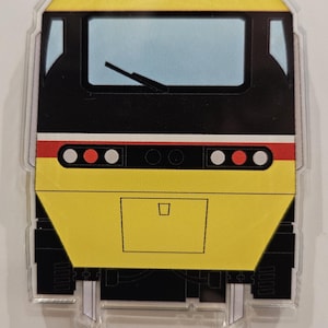 Puede incluir: Una pegatina con forma de tren amarillo y negro. La pegatina presenta una parte delantera amarilla con una parte superior e inferior negras. El tren tiene un parabrisas azul, luces rojas y blancas y ruedas negras. Un diseño divertido y colorido.