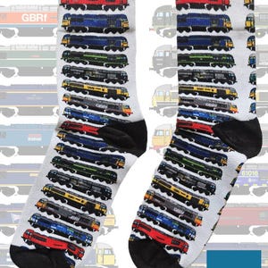 Könnte beinhalten: Ein Paar weiße Socken mit einem wiederkehrenden Muster aus verschiedenen Diesellokomotiven in den Farben Rot, Blau, Grün, Gelb und Schwarz. Die Socken haben schwarze Fersen und Zehenbereiche. Ein blaues Quadrat mit dem Text On The Rails ist zu sehen.