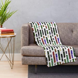 May include: A white throw blanket draped over a gray sofa, featuring a repeating pattern of colorful, vertical rectangles. The rectangles are in shades of red, green, blue, and black.