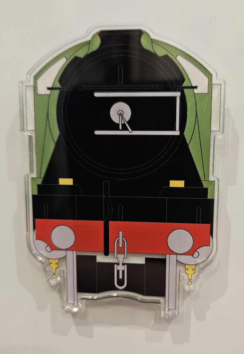 May include: A clear acrylic train-shaped ornament. The design features a black locomotive with green and red accents. The front of the train is black with a white gauge and a red bumper. The ornament is a cut-out shape.