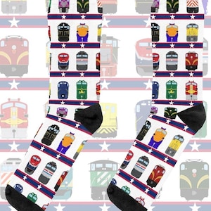 May include: A pair of white socks with a repeating pattern of colorful train illustrations. The socks feature black heels and toes, with red and blue stripes and white stars. The text "On The Rails" is visible.