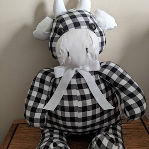 May include: A black and white gingham cow plush toy with a white bow. The toy has black eyes and a white face.