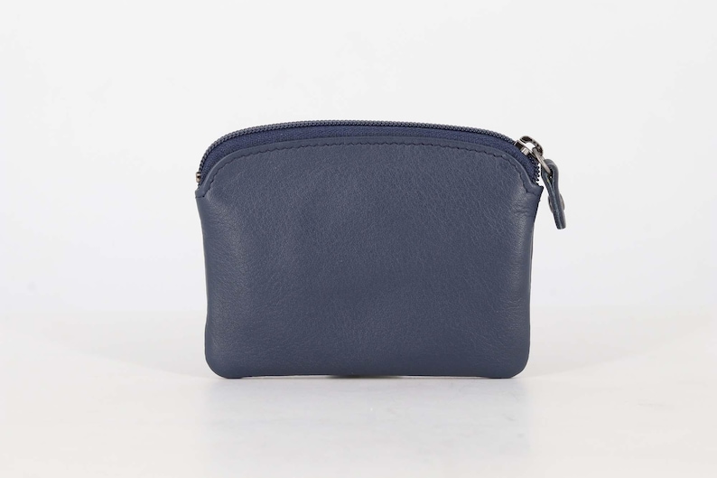 May include: A small, navy blue leather coin purse with a smooth texture and a rounded top edge. The pouch features a matching navy blue zipper closure along the top, complete with a small, rectangular leather pull tab attached to the metal slider.