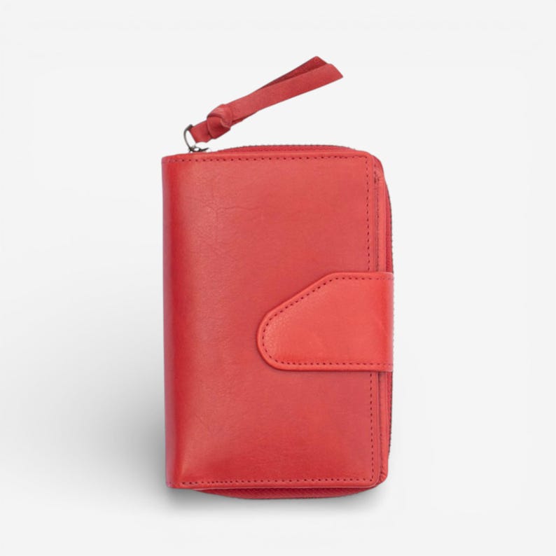 May include: A red leather wallet with a zip-around closure and a wrist strap. The wallet has a flap with a snap closure. The wallet is approximately 10 cm wide and 13 cm tall.