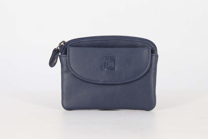 May include: A navy blue leather coin purse featuring a top zipper closure and a front flap pocket with a snap button. The front flap displays a small embossed logo. The purse has a rectangular shape with rounded corners and visible stitching.
