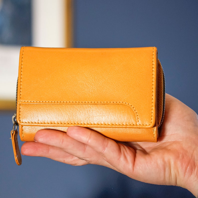 Yellow leather purse, size is shown by comparison to a woman's hand.