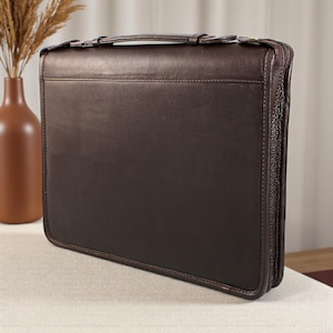 May include: A dark brown leather briefcase with a top handle and a secure clasp closure. The briefcase has a rectangular shape and a zipper closure around the edges. The leather appears smooth and has a slight sheen. The briefcase is designed for carrying documents and other items.