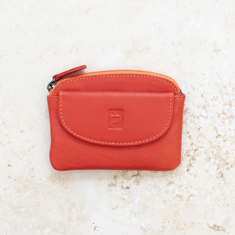 an orange leather coin purse with a zippered section which has a zipper puller and a front pocket.