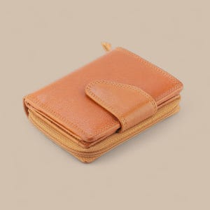 May include: A tan leather wallet featuring a textured surface, a central snap-button closure flap, and a wrap-around zipper along the perimeter. The wallet has a compact, rectangular shape with visible stitching along the edges and the closure flap.