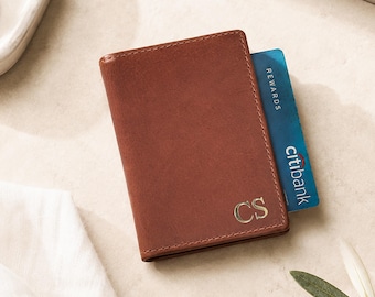 May include: A brown leather card holder featuring the gold embossed initials CS on the bottom right corner. A blue Citibank Rewards credit card is partially inserted into the top slot of the wallet, showing the bank name and rewards text.