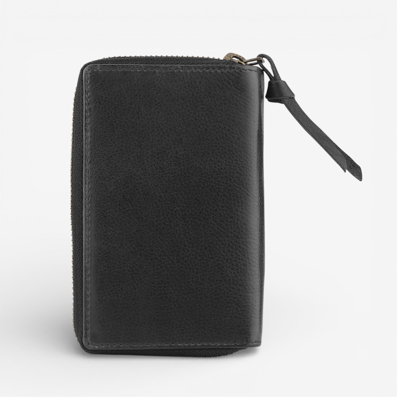 May include: A black leather wallet with a zip closure and a small leather pull tab. The wallet is rectangular and has a textured surface.
