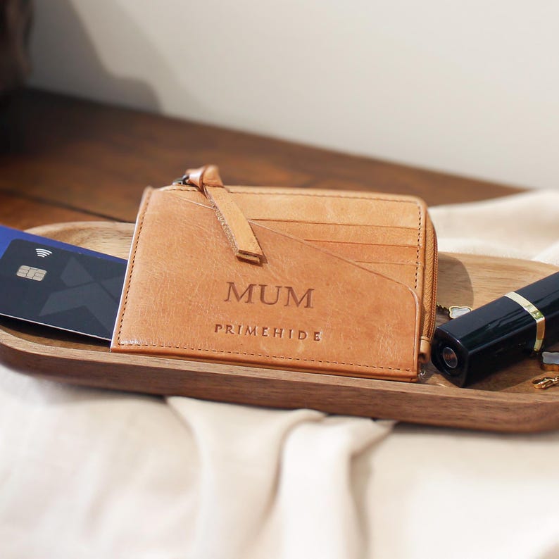 A tan leather wallet, embossed with "MUM" featuring a zip closure and card slots.
