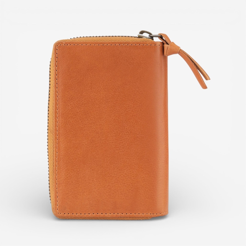 May include: A rectangular, tan leather wallet with a zip closure. The wallet features a small leather pull tab attached to the zip. The stitching is visible around the edges of the wallet.