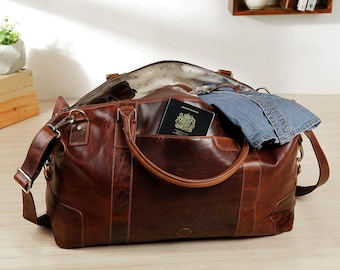 May include: A dark brown leather duffel bag with two top handles and a detachable shoulder strap. The bag is open, revealing a light-colored interior lining, a pair of folded blue denim jeans, and a black British passport tucked into a pocket.