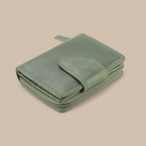 May include: A sage green bi-fold wallet with a textured leather surface, featuring a secure snap-button closure flap on the front and a wrap-around zipper that encloses the main compartment, providing a compact and functional design for storage.