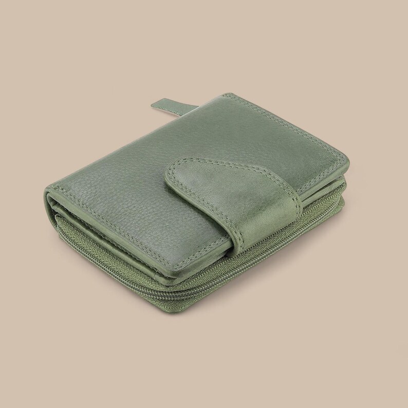 May include: A sage green bi-fold wallet with a textured leather surface, featuring a secure snap-button closure flap on the front and a wrap-around zipper that encloses the main compartment, providing a compact and functional design for storage.