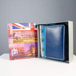 May include: A navy blue leather wallet with light blue contrast stitching, housed in a light gray box. The box lid features a Union Jack flag, the text RFID PROTECTED, and images of London landmarks including Big Ben and Tower Bridge.