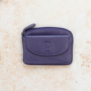 May include: A small purple leather coin purse featuring a top zipper closure and a front flap pocket with a debossed square logo. The rectangular pouch has rounded corners and a smooth finish, providing a compact storage solution for small items.