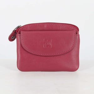 May include: A dark pink leather coin purse featuring a top zipper closure and a front flap pocket with a snap button. The front flap is embossed with a small square logo containing the letters 'pl'. The purse has a smooth, matte finish.