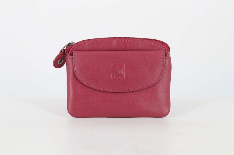 May include: A dark pink leather coin purse featuring a top zipper closure and a front flap pocket with a snap button. The front flap is embossed with a small square logo containing the letters 'pl'. The purse has a smooth, matte finish.
